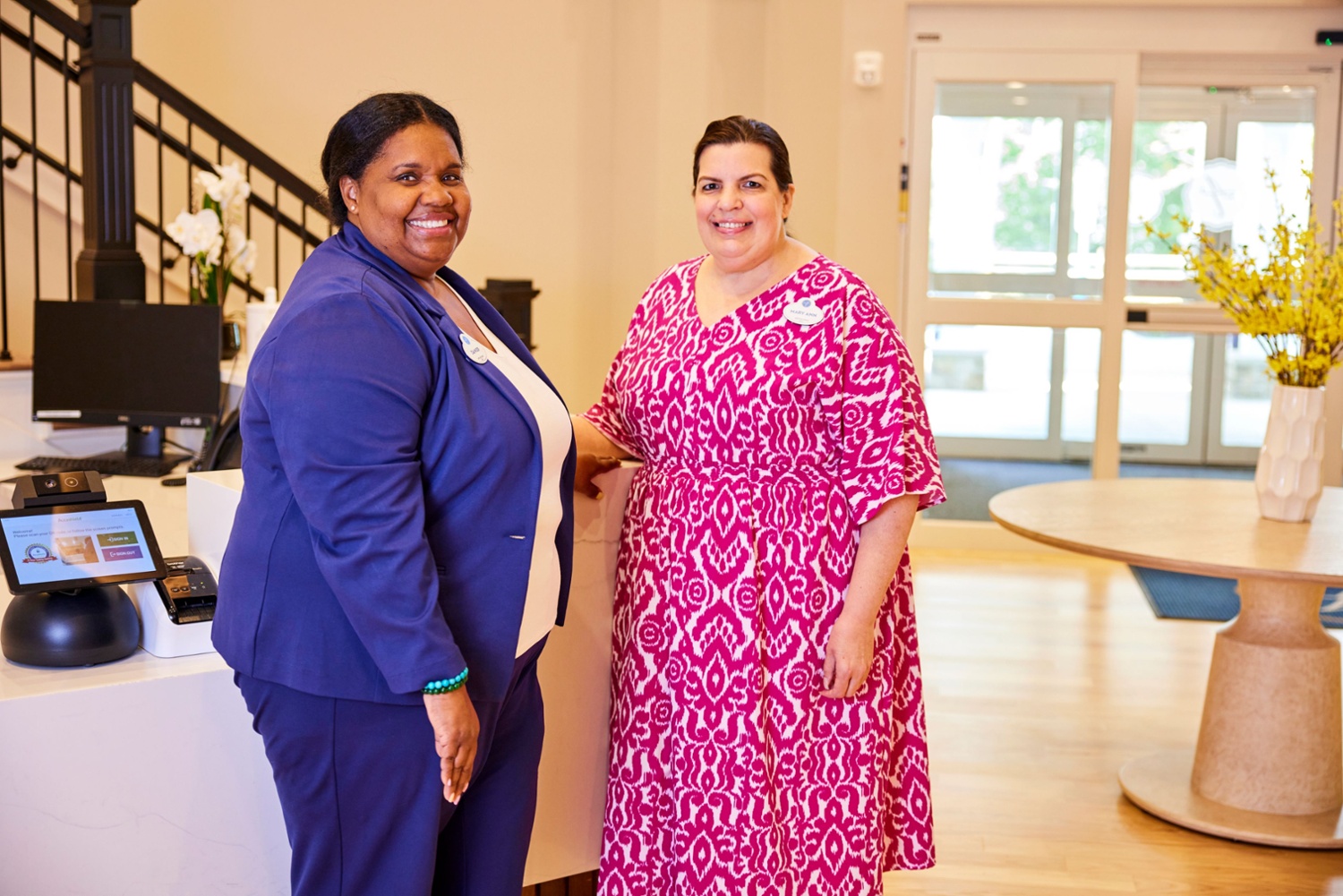two female arbor terrace employees in a purple and pink dress smiling